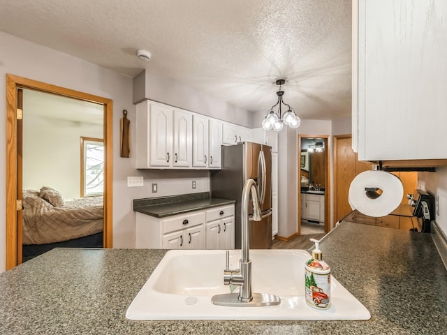 kitchen featuring pendant lighting, sink, stainless steel refrigerator with ice dispenser, a textured ceiling, and white cabinets