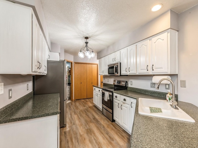 kitchen with sink, hanging light fixtures, stainless steel appliances, light hardwood / wood-style floors, and white cabinets