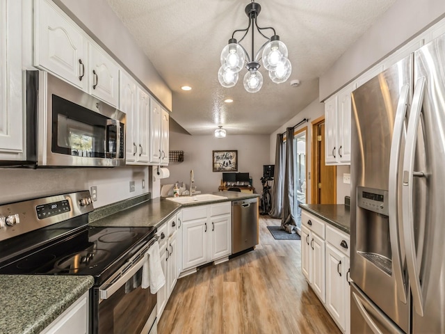 kitchen with sink, white cabinetry, hanging light fixtures, stainless steel appliances, and light wood-type flooring