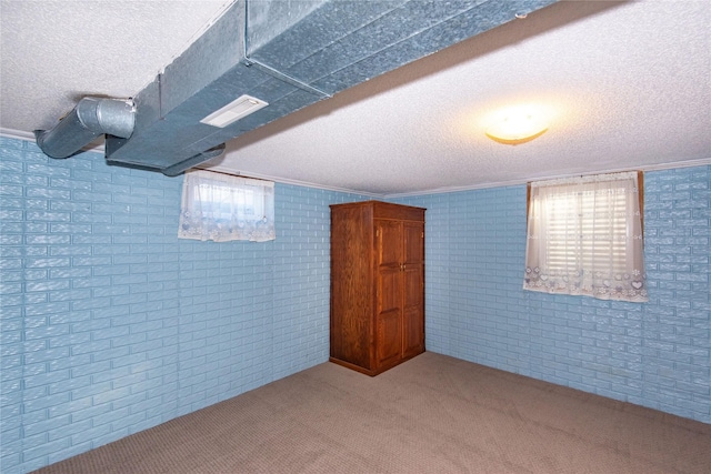 basement featuring a textured ceiling, brick wall, a healthy amount of sunlight, and carpet floors