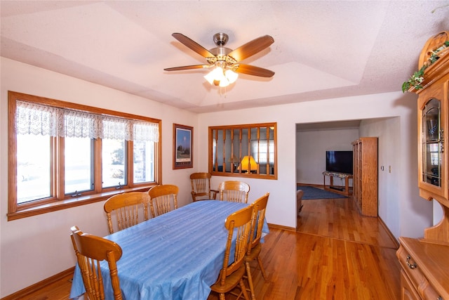 dining space featuring a raised ceiling, ceiling fan, and light hardwood / wood-style flooring