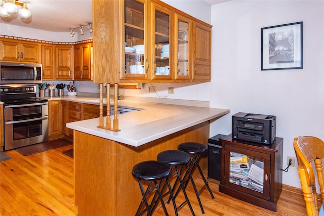 kitchen with a textured ceiling, appliances with stainless steel finishes, a kitchen breakfast bar, kitchen peninsula, and light wood-type flooring