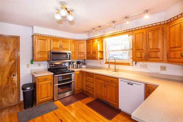 kitchen featuring light wood-type flooring, appliances with stainless steel finishes, a textured ceiling, and sink