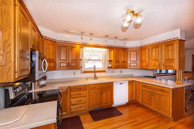 kitchen with kitchen peninsula, sink, light hardwood / wood-style flooring, appliances with stainless steel finishes, and a textured ceiling