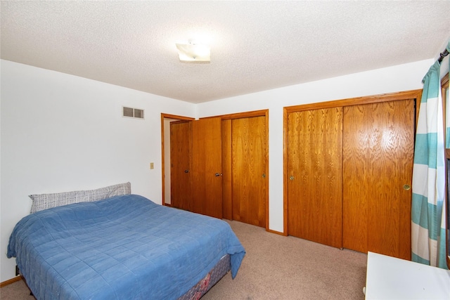 bedroom with light colored carpet, multiple closets, and a textured ceiling