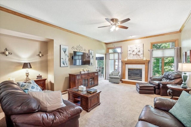 carpeted living room featuring ceiling fan, crown molding, and a tile fireplace