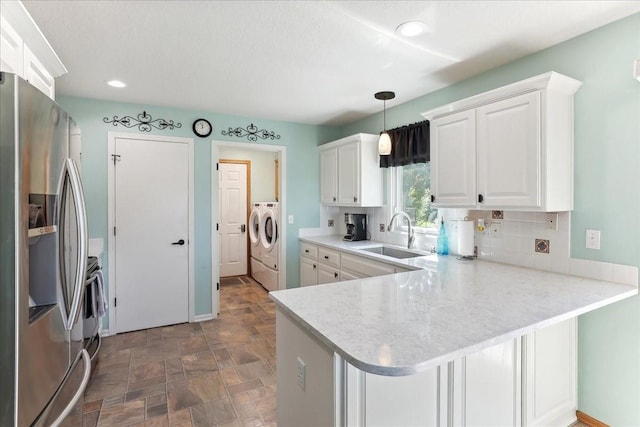 kitchen featuring washer and clothes dryer, white cabinets, sink, stainless steel fridge, and kitchen peninsula