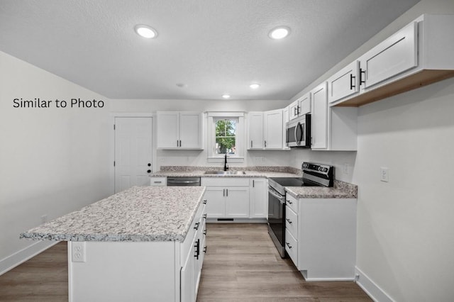 kitchen with white cabinets, appliances with stainless steel finishes, a center island, sink, and light wood-type flooring