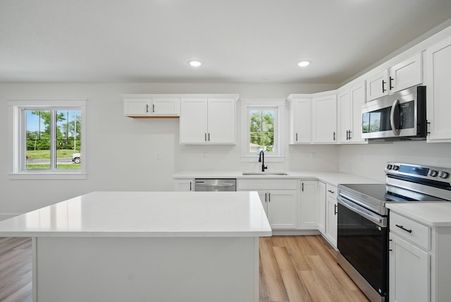2527 Shaw St, Des Moines, IA 50317 - kitchen featuring stainless steel appliances, a sink, light wood-style floors, white cabinetry, and a center island