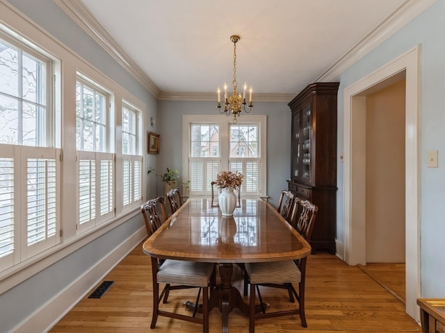 dining room with light wood-type flooring, crown molding, and an inviting chandelier