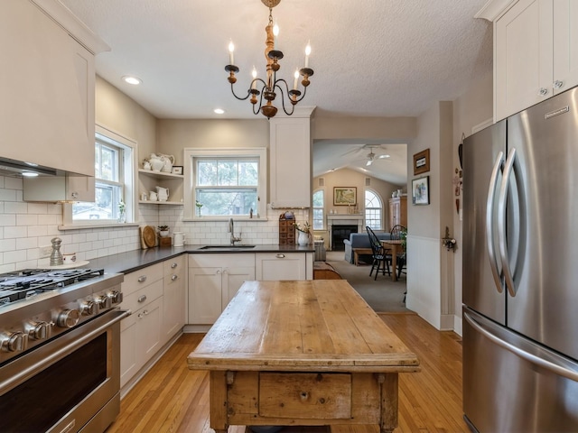 kitchen featuring lofted ceiling, sink, appliances with stainless steel finishes, white cabinets, and ceiling fan with notable chandelier