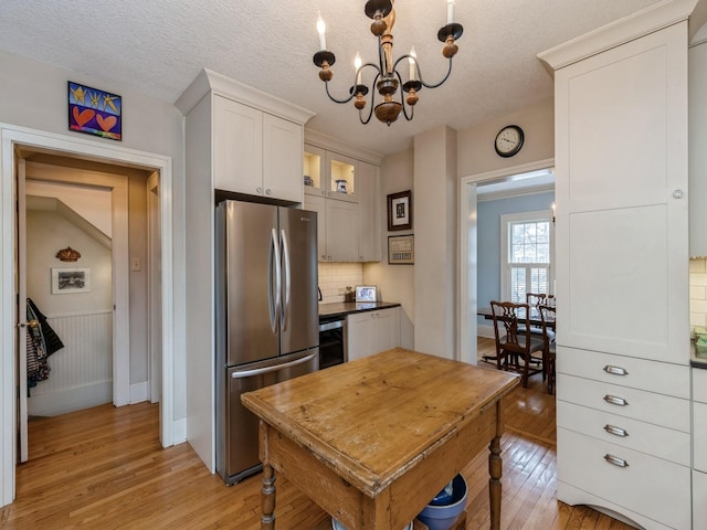 kitchen featuring a textured ceiling, white cabinets, a notable chandelier, stainless steel refrigerator, and light hardwood / wood-style flooring