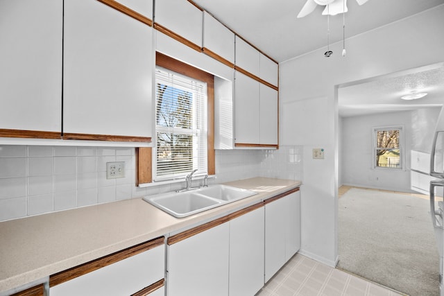 kitchen featuring ceiling fan, tasteful backsplash, sink, light carpet, and white cabinets