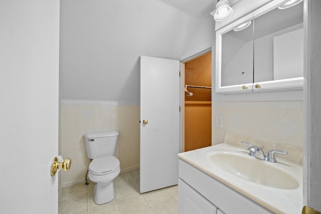 bathroom featuring toilet, tile patterned flooring, tile walls, vaulted ceiling, and vanity