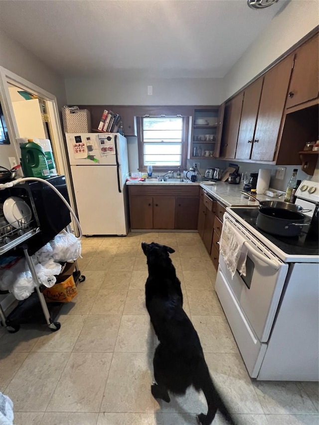 kitchen with light tile patterned floors, sink, white appliances, and dark brown cabinetry