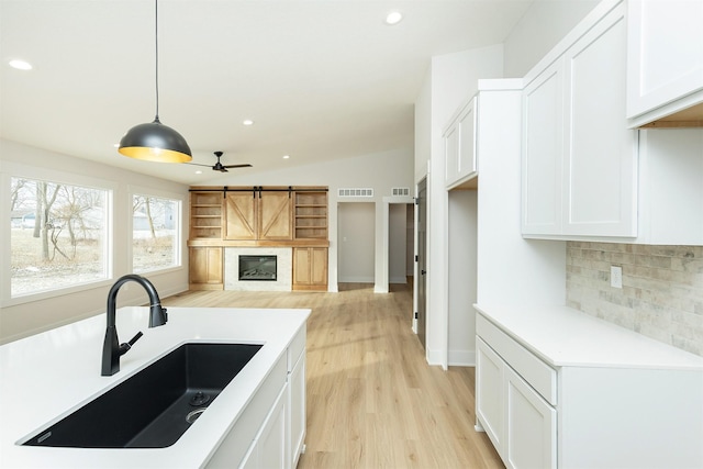 2390 Emma Ave, Des Moines, IA 50321 - kitchen with backsplash, a glass covered fireplace, white cabinetry, light wood-type flooring, and ceiling fan