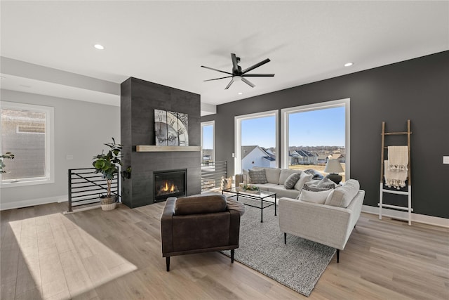 living room featuring ceiling fan, a tile fireplace, and light hardwood / wood-style floors