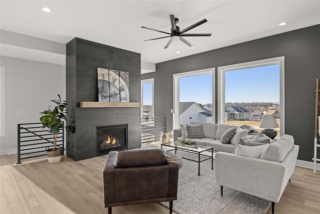 living room featuring ceiling fan, a wealth of natural light, a fireplace, and light hardwood / wood-style flooring