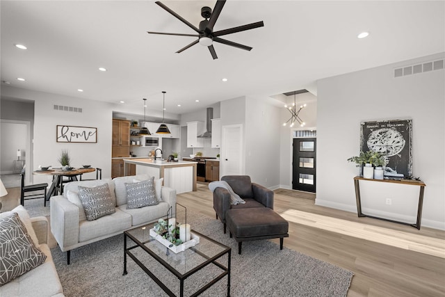 living room featuring sink, ceiling fan with notable chandelier, and light hardwood / wood-style floors