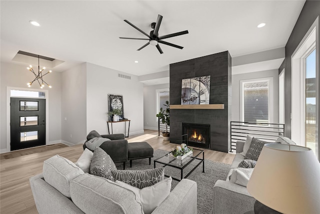 living room featuring light wood-type flooring, a tile fireplace, and ceiling fan with notable chandelier