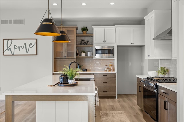 kitchen featuring stainless steel appliances, backsplash, white cabinets, pendant lighting, and light hardwood / wood-style flooring