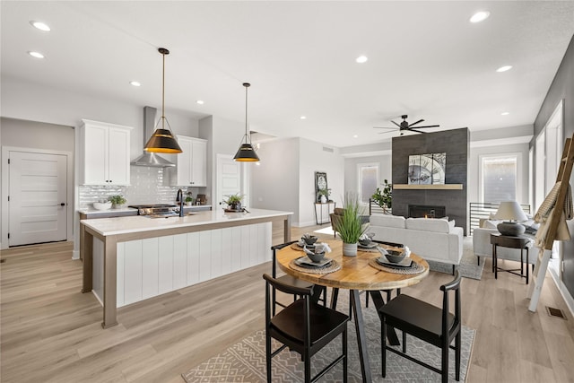 kitchen featuring white cabinetry, an island with sink, tasteful backsplash, pendant lighting, and light hardwood / wood-style flooring