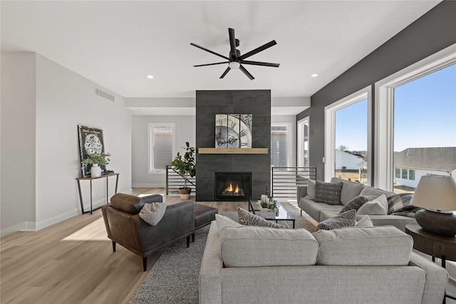 living room featuring ceiling fan, light hardwood / wood-style flooring, and a tiled fireplace