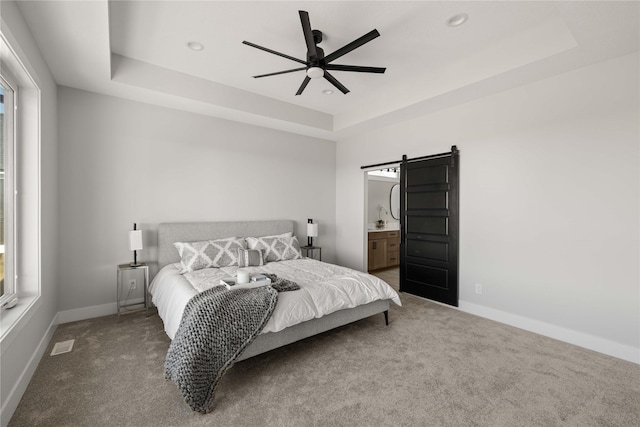 bedroom featuring connected bathroom, ceiling fan, a barn door, and a tray ceiling