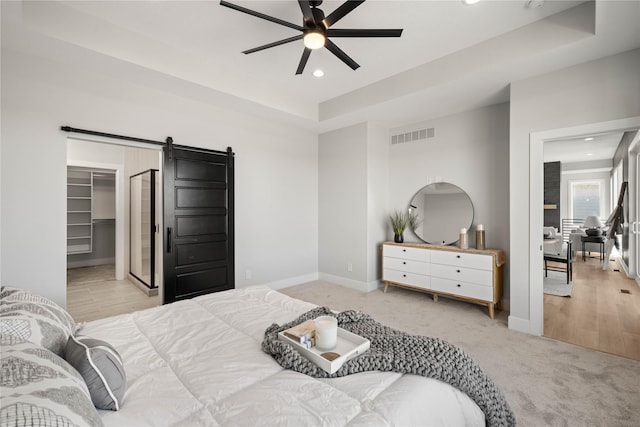 bedroom featuring light carpet, a barn door, ceiling fan, a closet, and a walk in closet