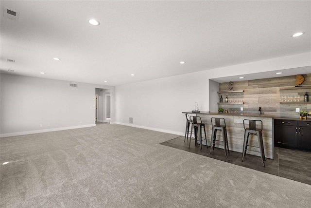 kitchen with a breakfast bar, sink, wooden walls, and dark carpet