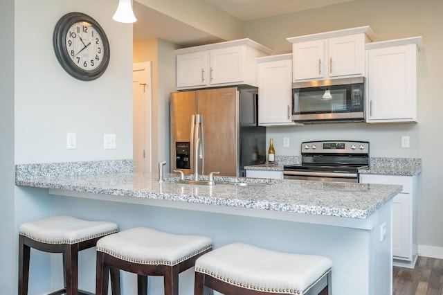 kitchen with kitchen peninsula, white cabinetry, dark wood-type flooring, light stone countertops, and stainless steel appliances