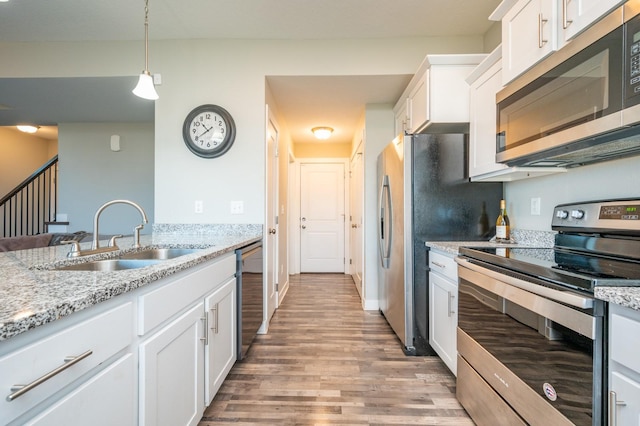 kitchen with white cabinets, appliances with stainless steel finishes, sink, hanging light fixtures, and light stone counters