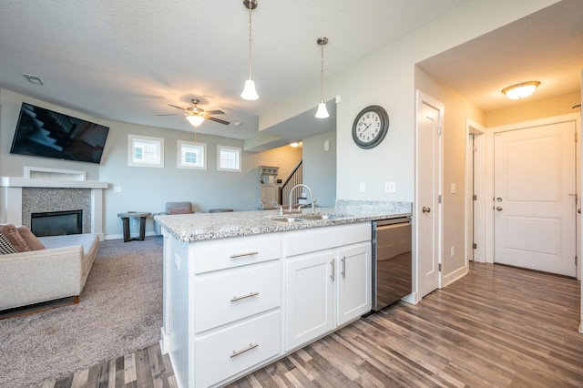 kitchen featuring dishwasher, hanging light fixtures, light stone countertops, white cabinets, and a tile fireplace