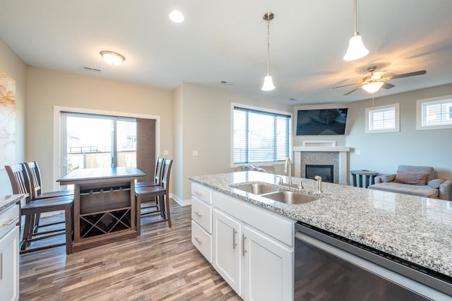 kitchen with white cabinetry, wood-type flooring, light stone countertops, pendant lighting, and sink