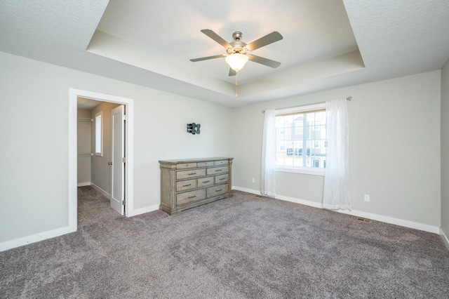 unfurnished bedroom featuring ceiling fan, a spacious closet, carpet floors, and a tray ceiling