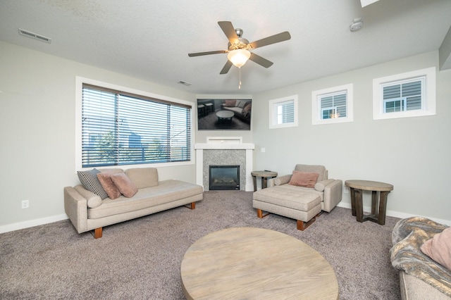 living room with a textured ceiling, ceiling fan, carpet flooring, and a tile fireplace