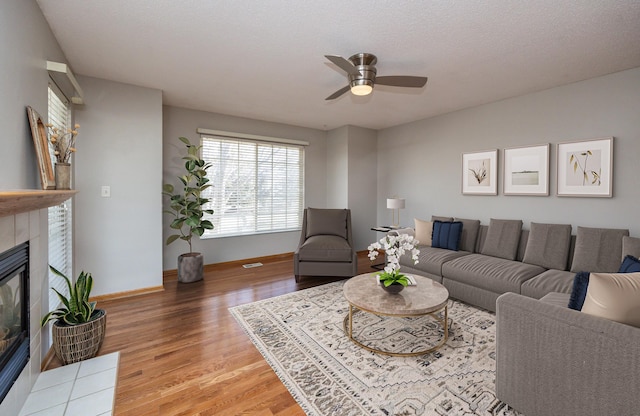 living room with a tile fireplace, wood-type flooring, a textured ceiling, and ceiling fan