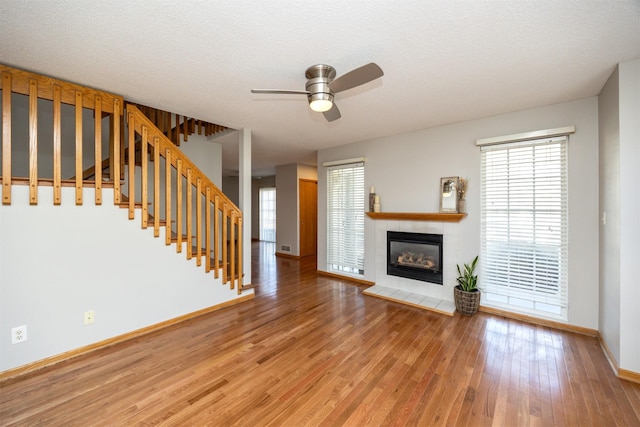 unfurnished living room with stairs, a tiled fireplace, light wood-type flooring, and a wealth of natural light