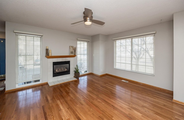 unfurnished living room featuring wood finished floors, visible vents, baseboards, a textured ceiling, and a tiled fireplace