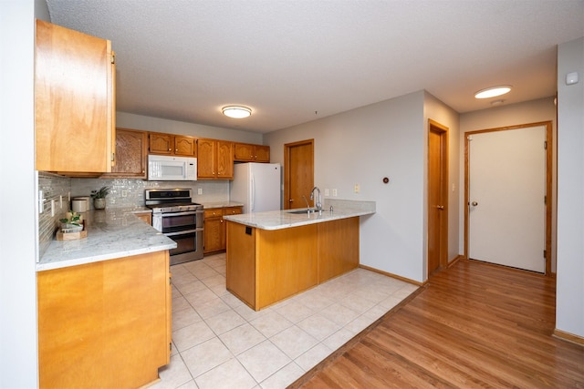 kitchen featuring decorative backsplash, brown cabinets, a peninsula, white appliances, and a sink