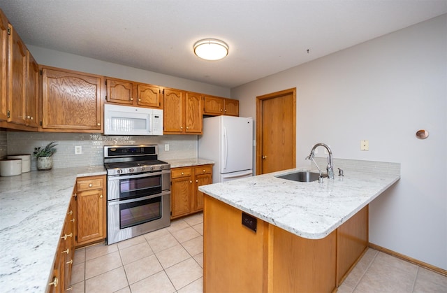 kitchen featuring a sink, backsplash, white appliances, a peninsula, and light tile patterned flooring