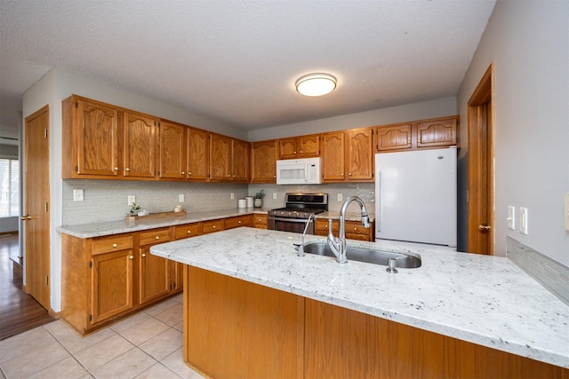 kitchen featuring a sink, white appliances, brown cabinetry, light tile patterned floors, and light stone countertops