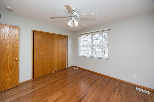 unfurnished bedroom featuring wood finished floors, visible vents, a closet, and baseboards