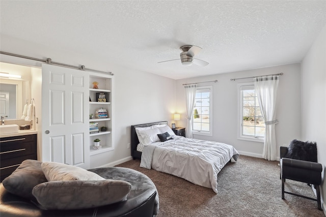 bedroom with ceiling fan, a barn door, sink, a textured ceiling, and dark colored carpet