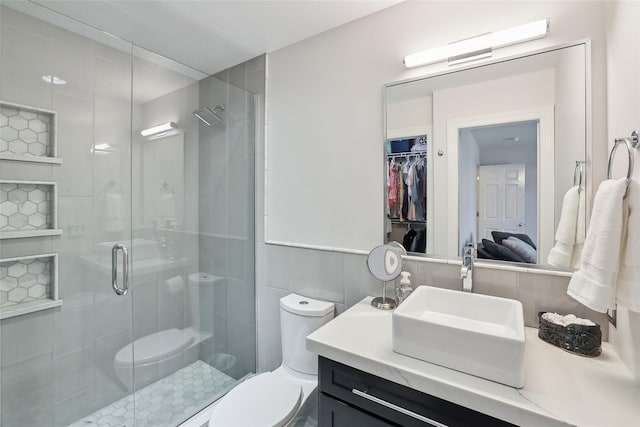 bathroom with tile walls, a stall shower, vanity, toilet, and a spacious closet
