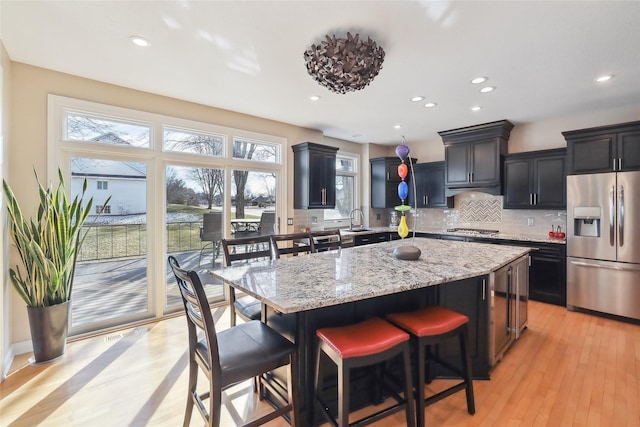 kitchen with stainless steel appliances, a kitchen breakfast bar, light stone countertops, a kitchen island, and sink