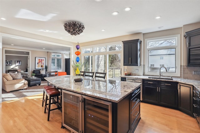 kitchen featuring light hardwood / wood-style floors, a center island, wine cooler, a breakfast bar, and sink