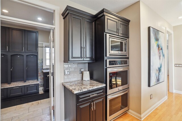 kitchen featuring backsplash, appliances with stainless steel finishes, light stone counters, and light hardwood / wood-style flooring