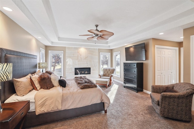 bedroom with a fireplace, a closet, carpet flooring, ceiling fan, and a tray ceiling