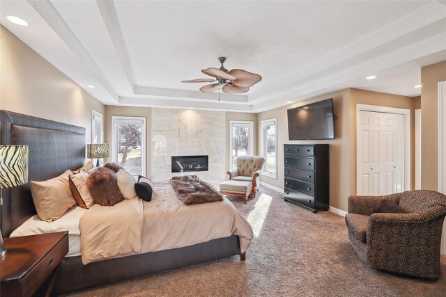 bedroom with a raised ceiling, multiple windows, carpet, and a tile fireplace
